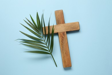 Photo of Wooden cross and palm leaf on light blue background, top view. Easter attributes