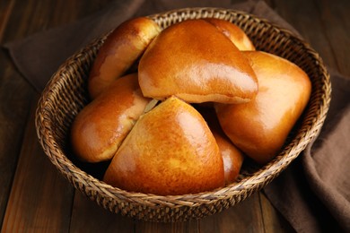 Photo of Wicker basket with delicious baked pirozhki on wooden table