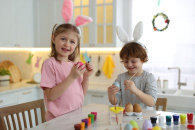 Easter celebration. Cute children with bunny ears painting eggs at white marble table in kitchen