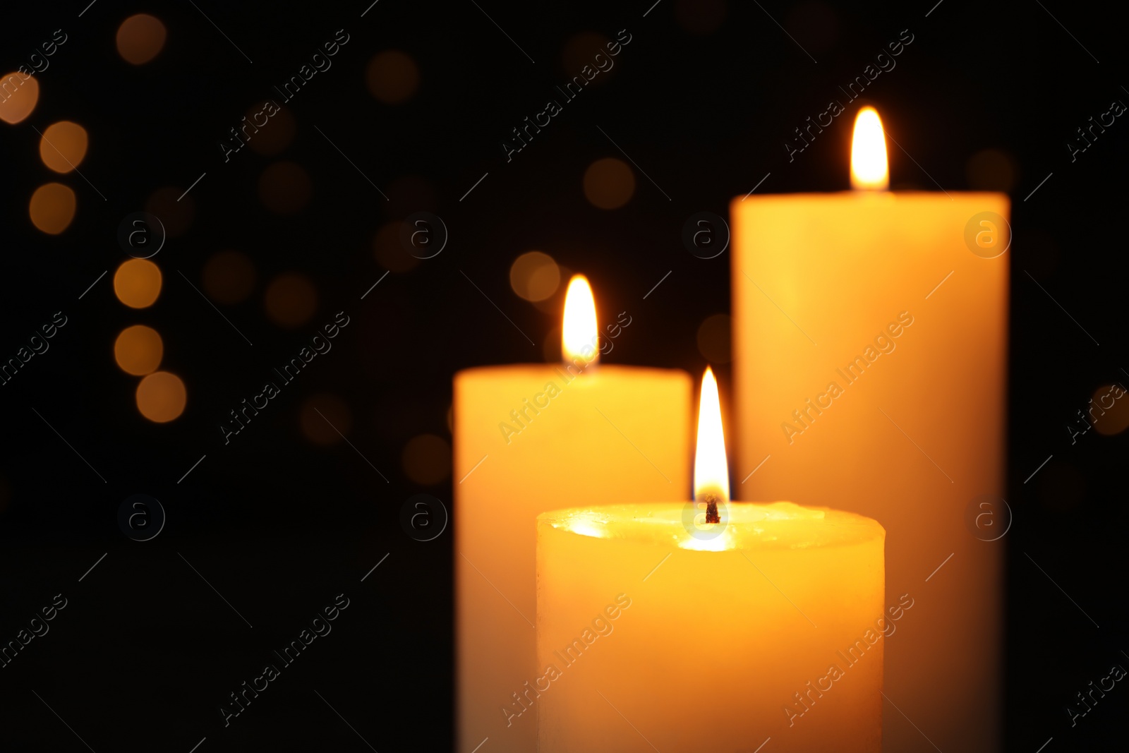 Photo of Burning candles on black background with blurred lights, space for text