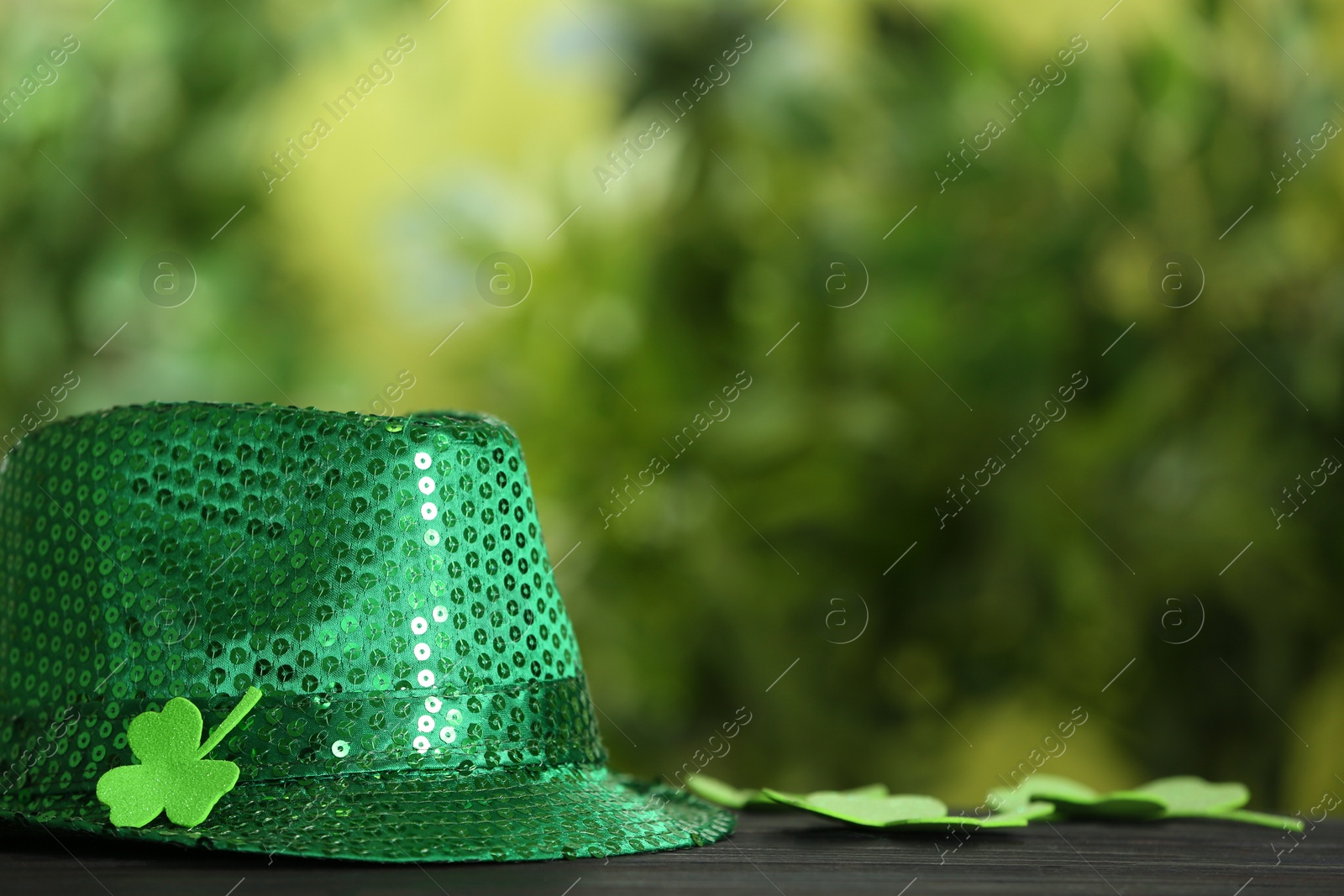 Photo of Green sequin hat with clover leaf on wooden table against blurred background, space for text. St Patrick's Day celebration