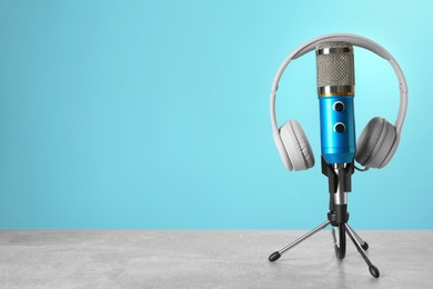Microphone and modern headphones on grey table against light blue background, space for text