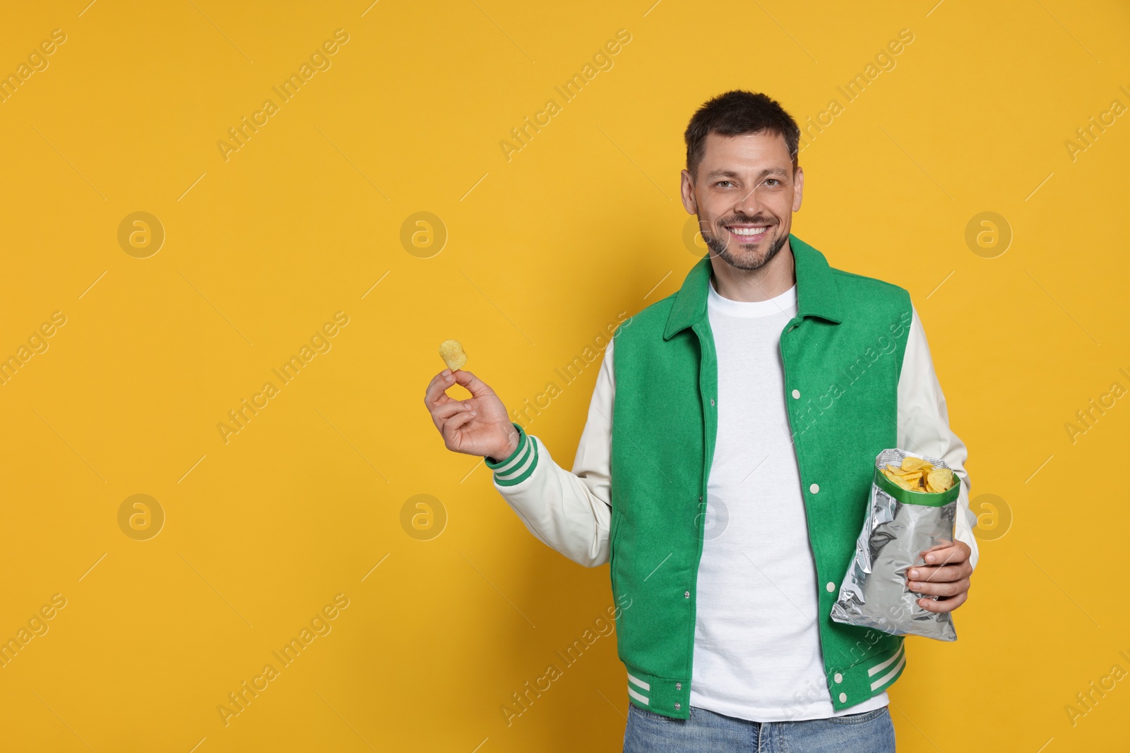 Photo of Handsome man with potato chips on orange background, space for text