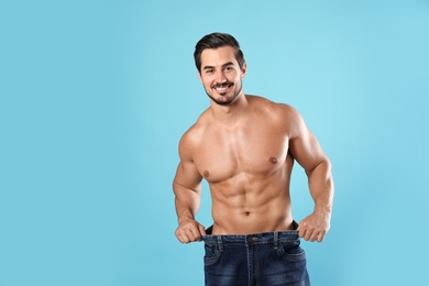 Photo of Young man with slim body in old big size jeans on light blue background. Space for text