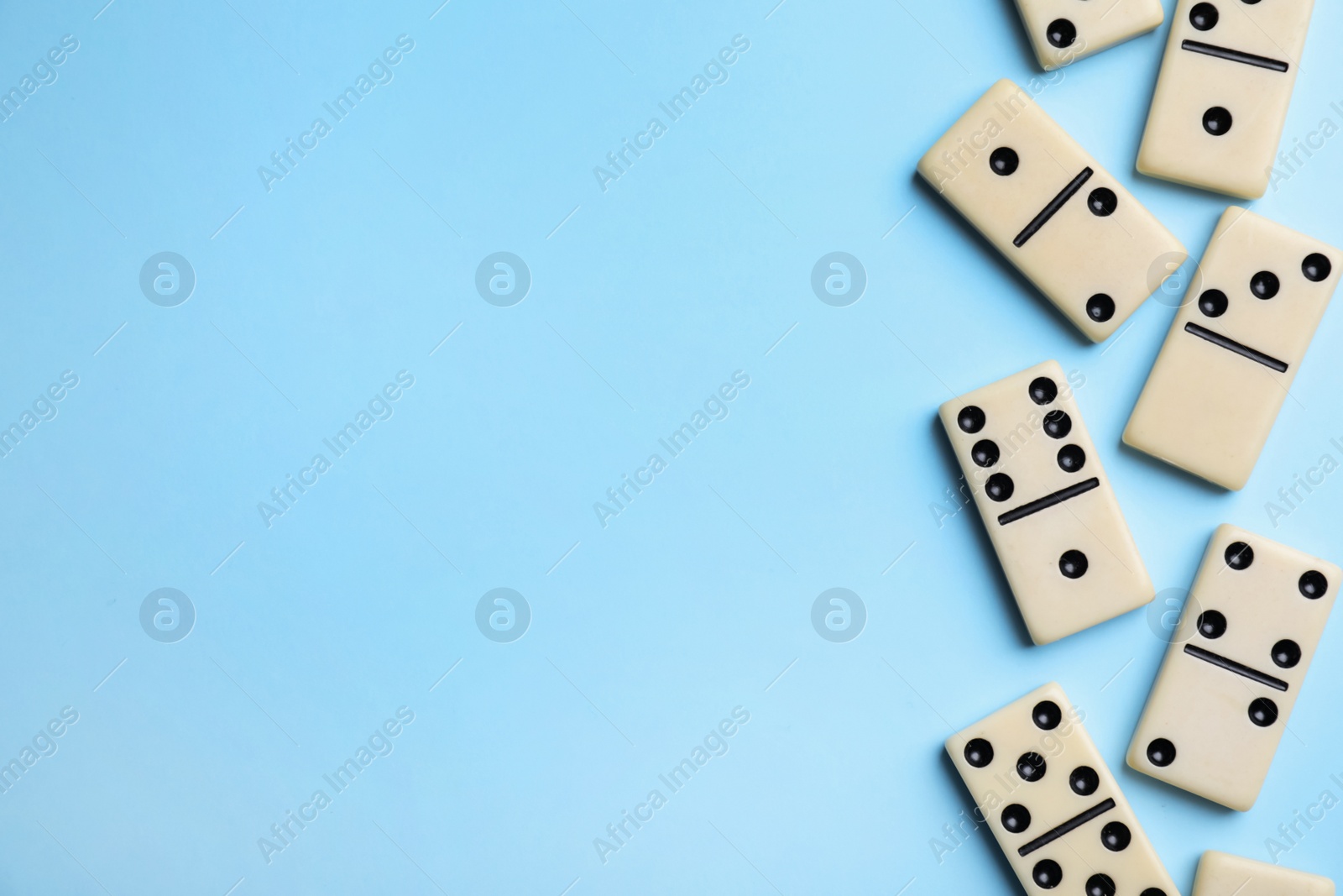 Photo of Classic domino tiles on light blue background, flat lay. Space for text