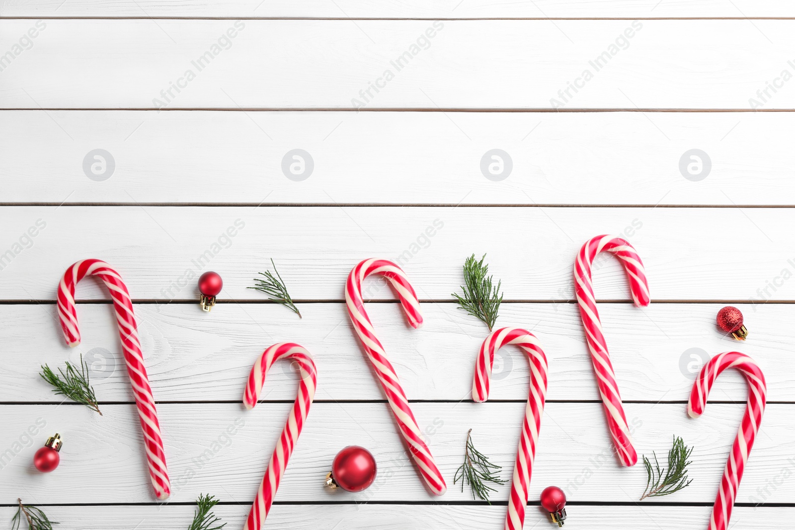 Photo of Candy canes, fir branches and Christmas balls on white wooden table, flat lay. Space for text