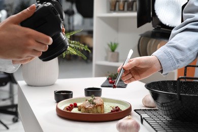 Photo of Professional photographer taking photo while food stylist decorating composition with meat medallion in studio, closeup