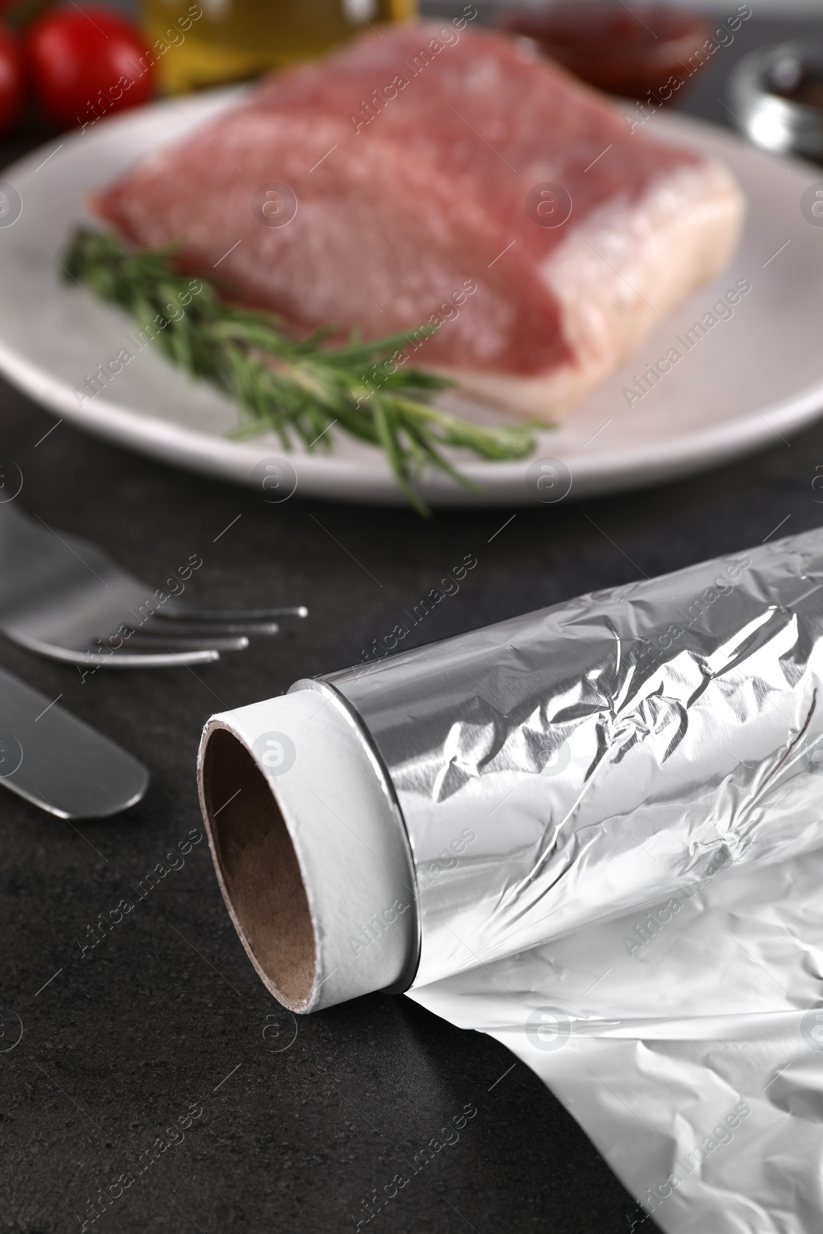 Photo of Aluminum foil, products and raw meat on dark table, closeup