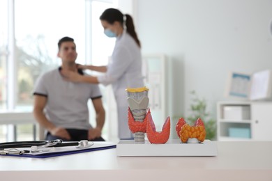 Photo of Doctor examining patient in office, focus on plastic model of healthy and afflicted thyroids