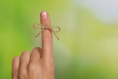 Photo of Woman showing index finger with tied bow as reminder on green blurred background, closeup. Space for text