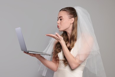 Beautiful bride with laptop blowing kiss on gray background