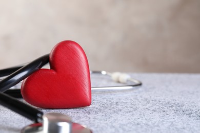 Photo of Stethoscope and red heart on grey stone table. Space for text