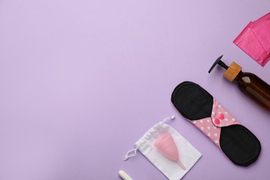 Photo of Cloth menstrual pad and other female hygiene products on violet background, flat lay. Space for text