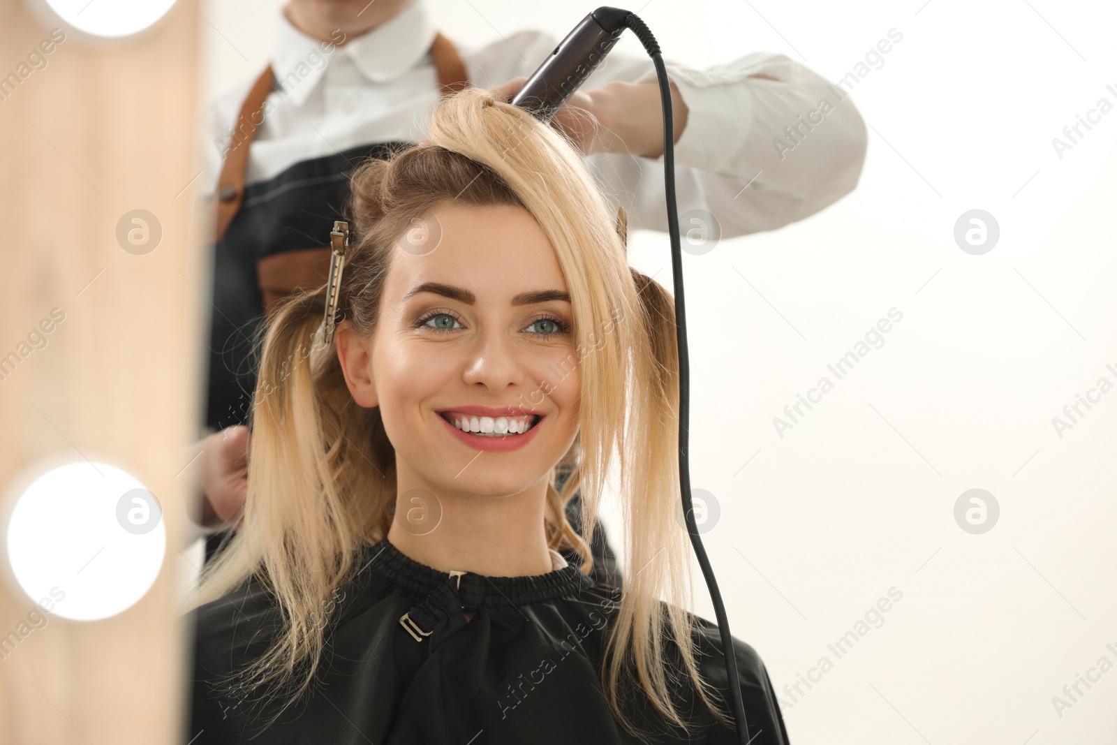 Photo of Hair styling. Hairdresser curling woman's hair in salon, closeup