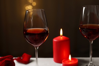 Glasses of red wine, burning candles and rose flower on grey table against blurred lights. Romantic atmosphere