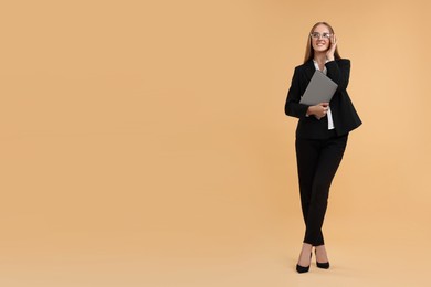 Happy young secretary with laptop on beige background, space for text