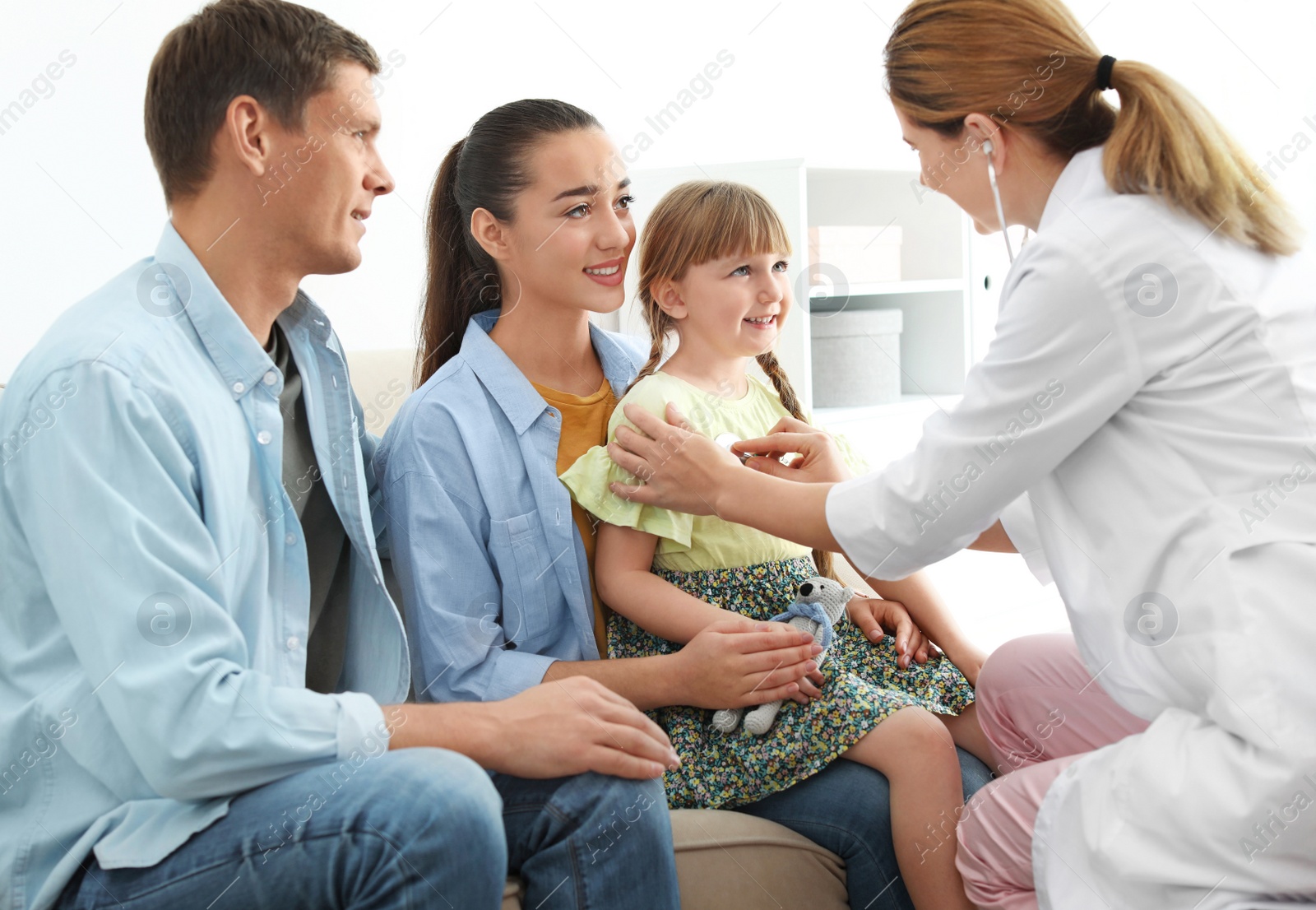 Photo of Children's doctor examining little girl near parents at home. House call