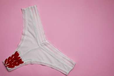 Photo of Woman's panties with red flower petals on pink background, top view. Space for text