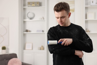 Photo of Pet shedding. Man with lint roller removing dog's hair from sweater at home. Space for text