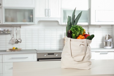 Photo of Textile shopping bag full of vegetables on table in kitchen. Space for text