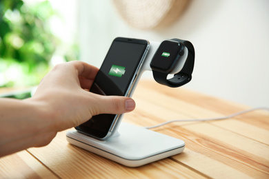 Photo of Man putting mobile phone onto wireless charger at wooden table, closeup. Modern workplace accessory