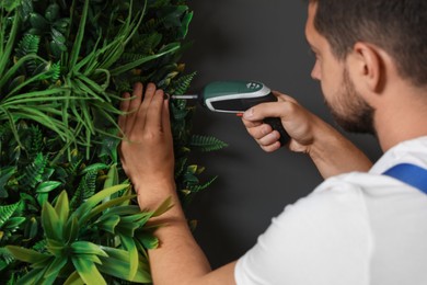 Man with screwdriver installing green artificial plant panel on grey wall, closeup