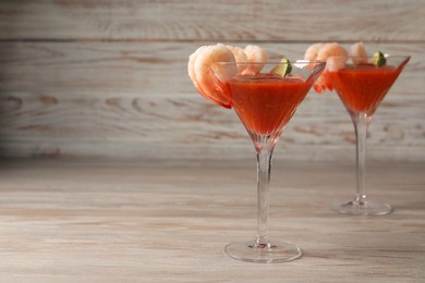 Photo of Tasty shrimp cocktail with sauce and lime in glasses on wooden table, space for text