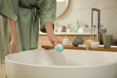 Photo of Young woman holding bath bomb over tub in bathroom, closeup