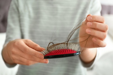 Photo of Woman holding brush with fallen long hair, closeup