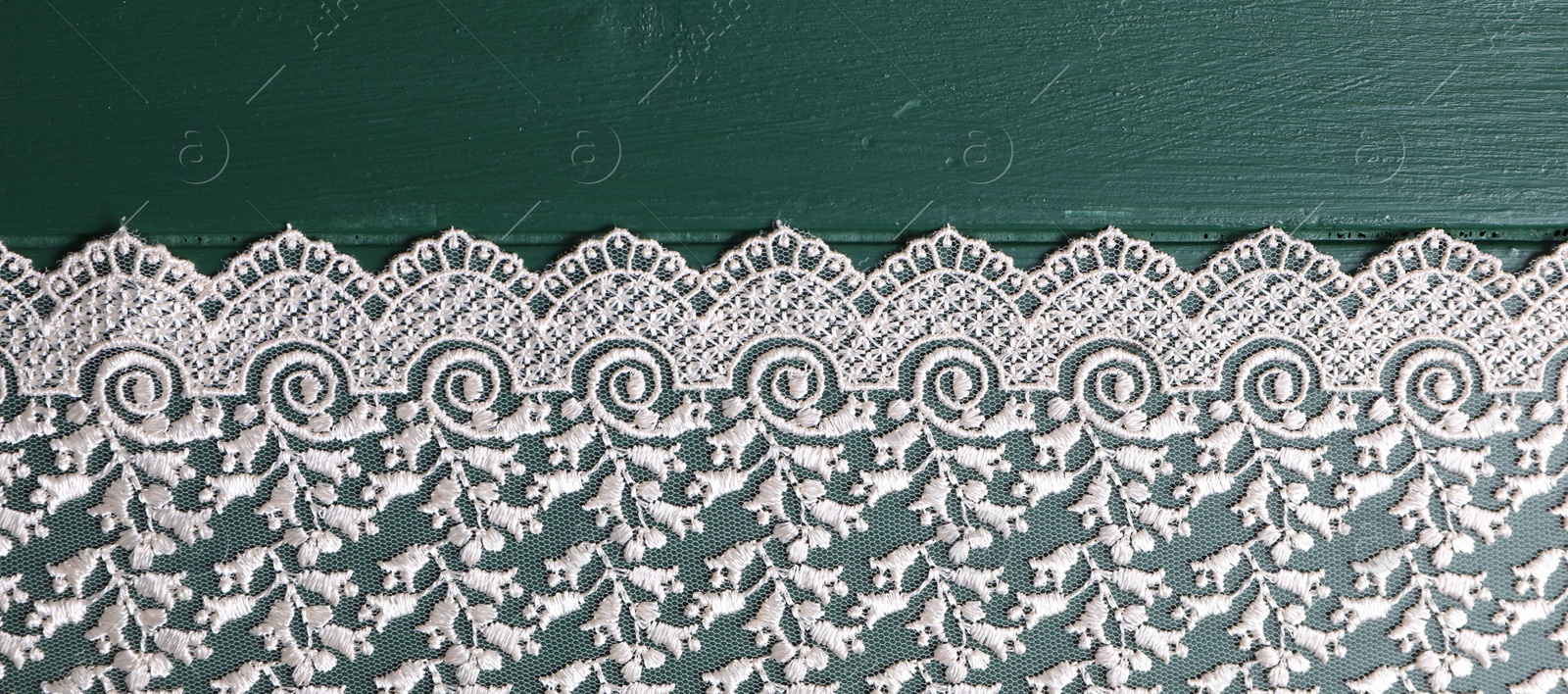 Photo of Beige lace on green wooden table, top view