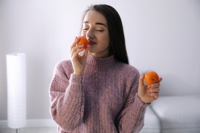 Photo of Happy young woman with fresh ripe tangerines at home