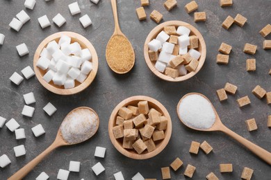 Photo of Bowls and spoons with different types of sugar on gray table, flat lay