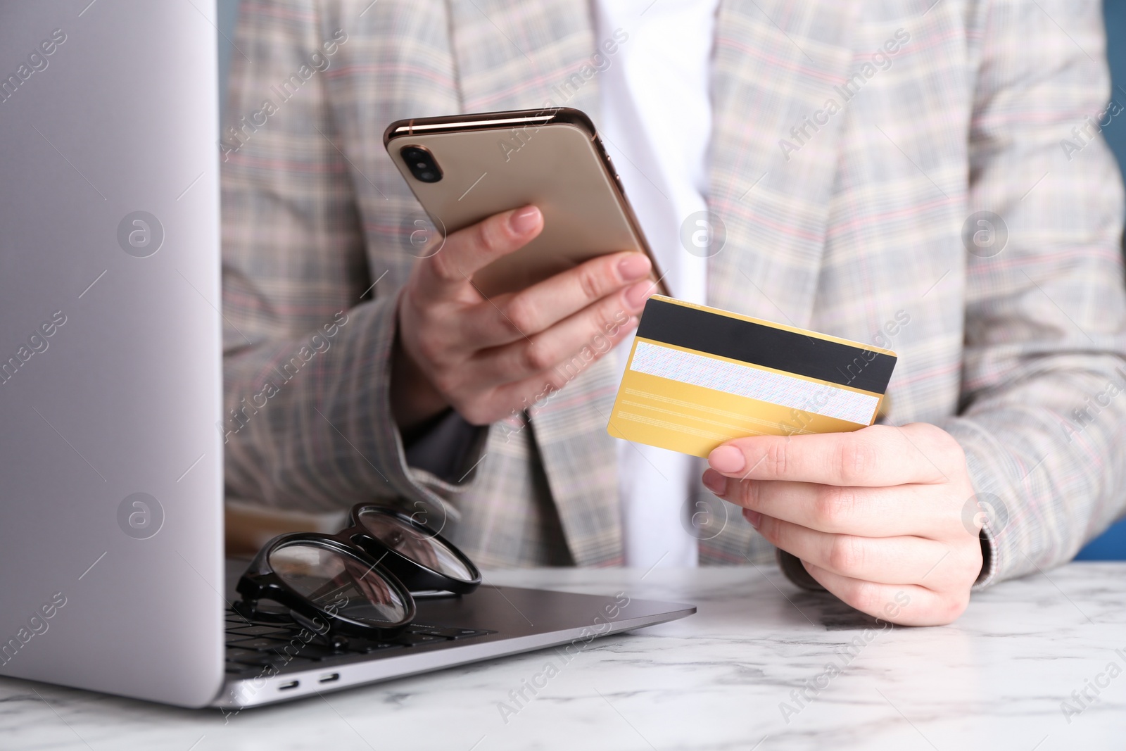 Photo of Online payment. Woman with laptop, smartphone and credit card at white marble table, closeup