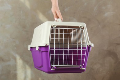 Photo of Woman holding violet pet carrier against grey wall, closeup