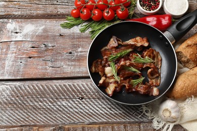 Photo of Delicious bacon slices in frying pan and products on wooden table, flat lay. Space for text