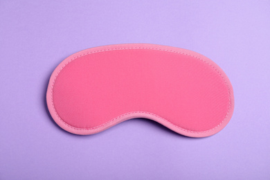 Photo of Pink sleeping mask on violet background, top view. Bedtime accessory