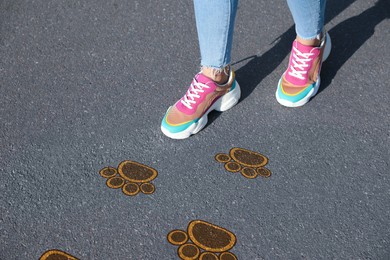 Planning future. Woman walking on drawn marks on road, closeup. Animal paw prints showing direction of way