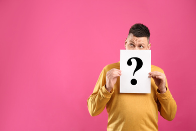 Photo of Emotional man holding paper with question mark on pink background, space for text