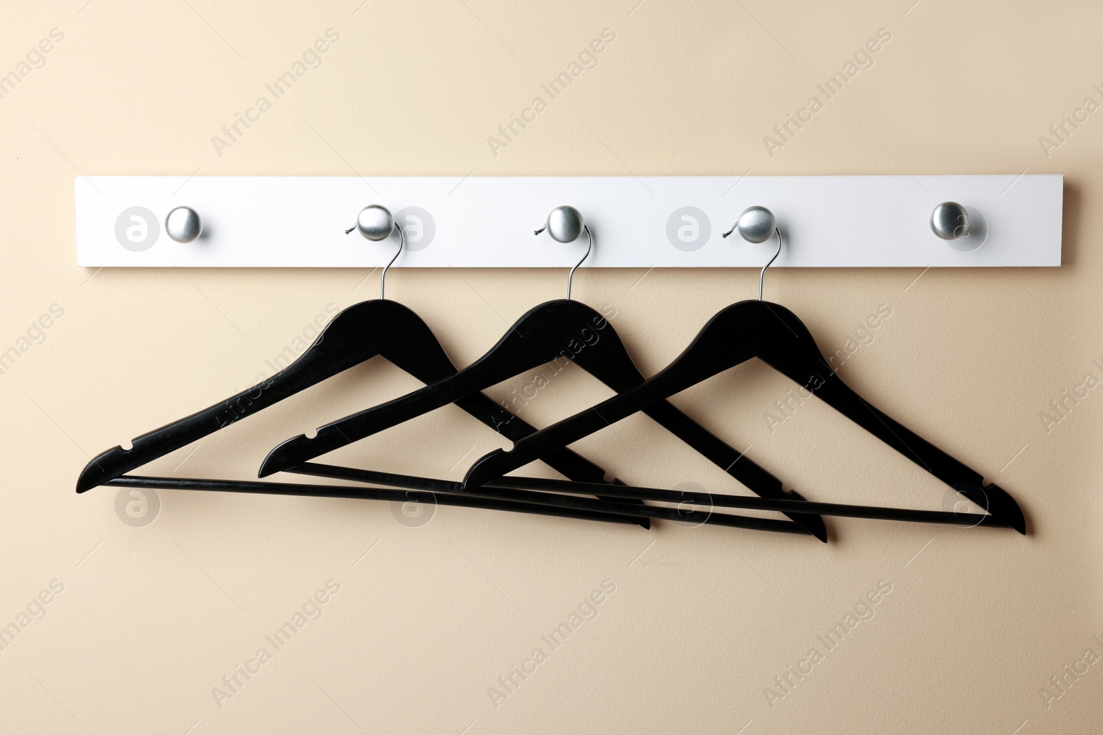 Photo of Rack with empty black clothes hangers on beige wall