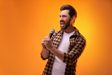 Photo of Handsome man with microphone singing on golden background. Space for text