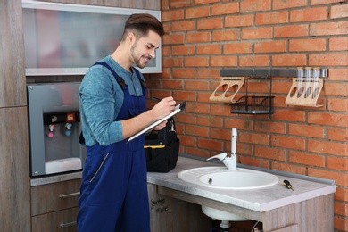 Male plumber with clipboard near kitchen sink. Repair service