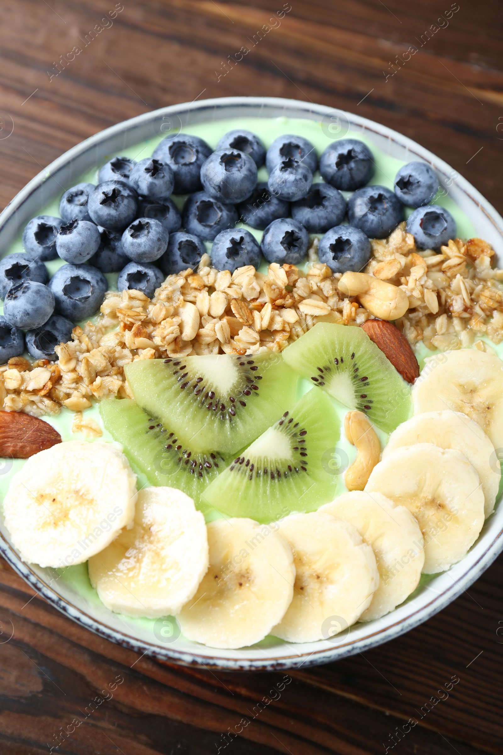 Photo of Tasty smoothie bowl with fresh fruits and oatmeal on wooden table, above view