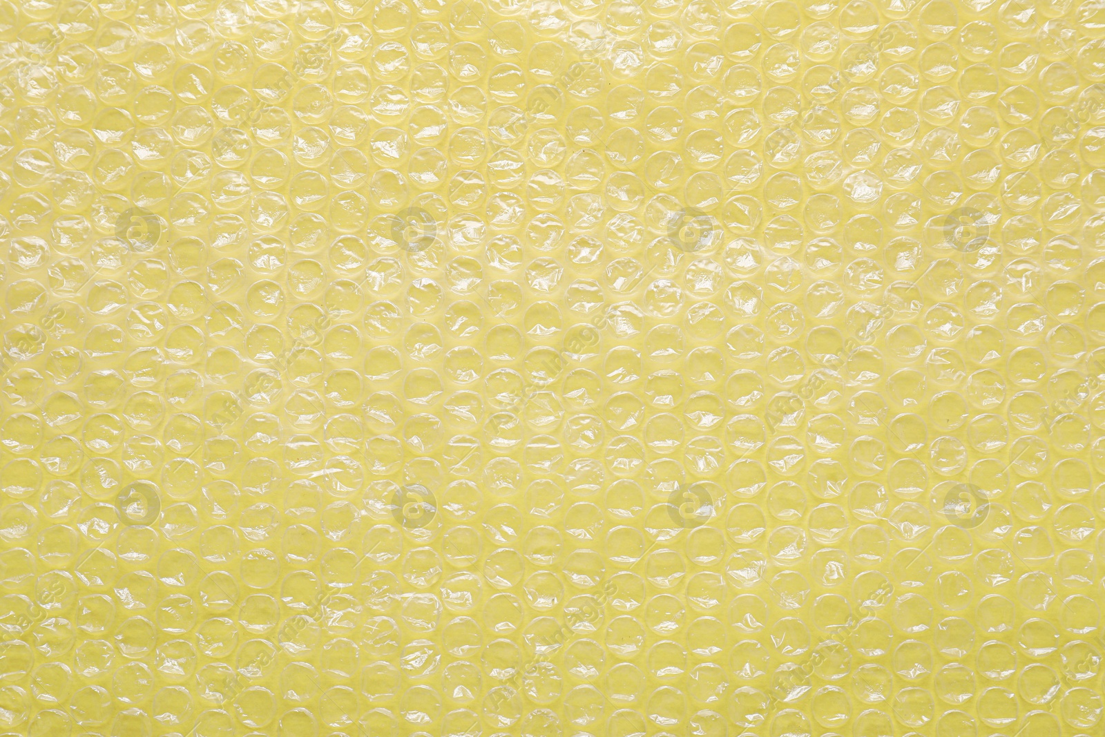 Photo of Transparent bubble wrap on yellow background, top view