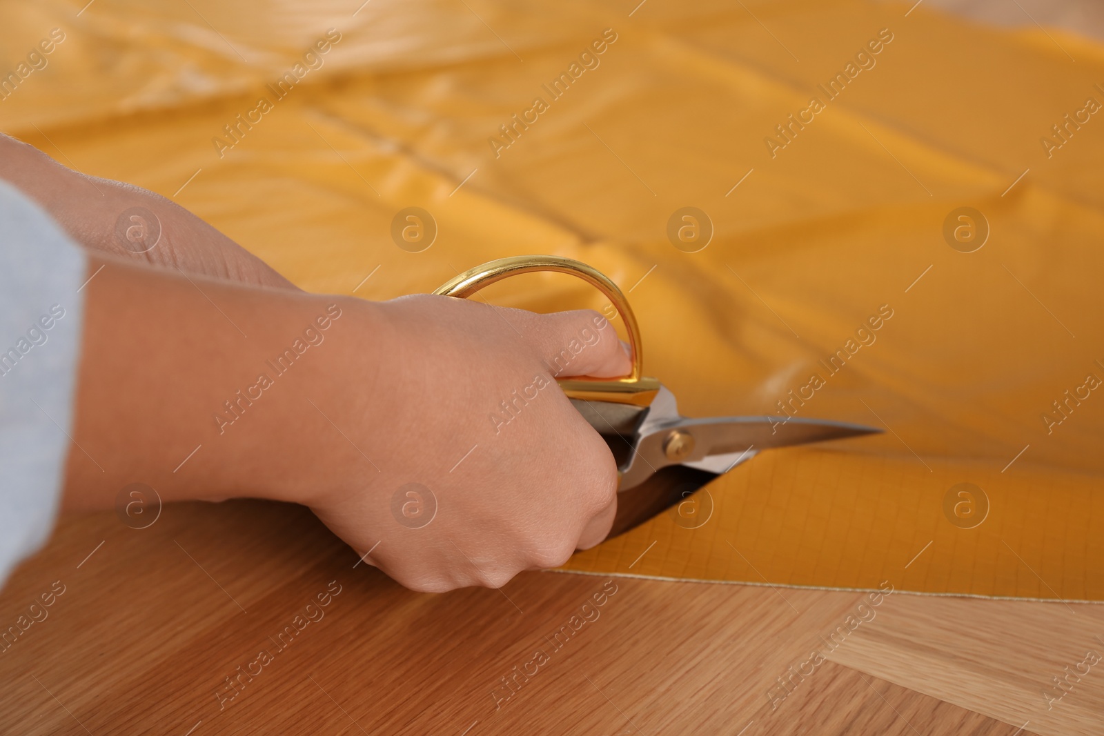 Photo of Woman cutting orange leather with scissors at wooden table, closeup