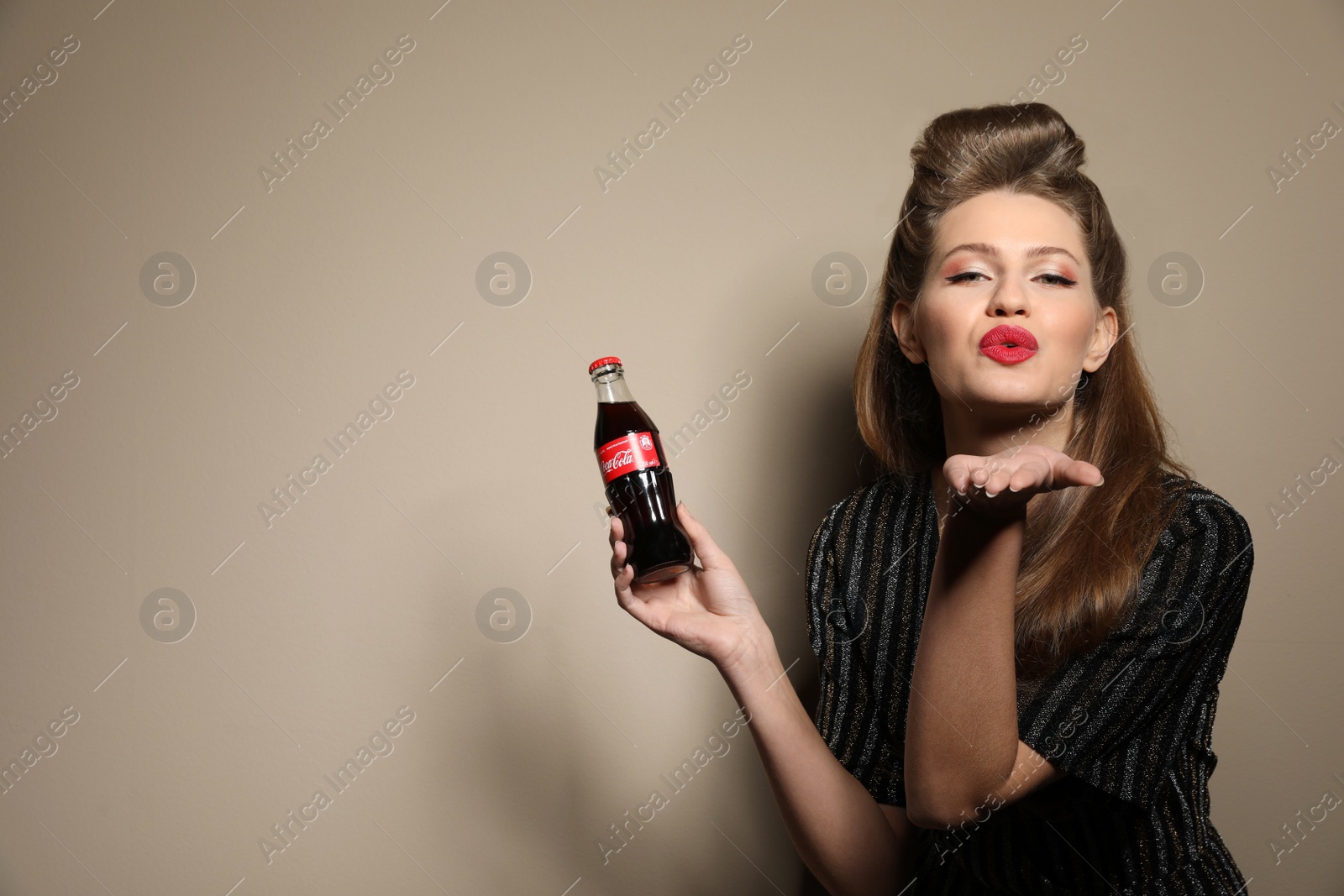 Photo of MYKOLAIV, UKRAINE - NOVEMBER 28, 2018: Young woman with bottle of Coca-Cola on color background, space for text