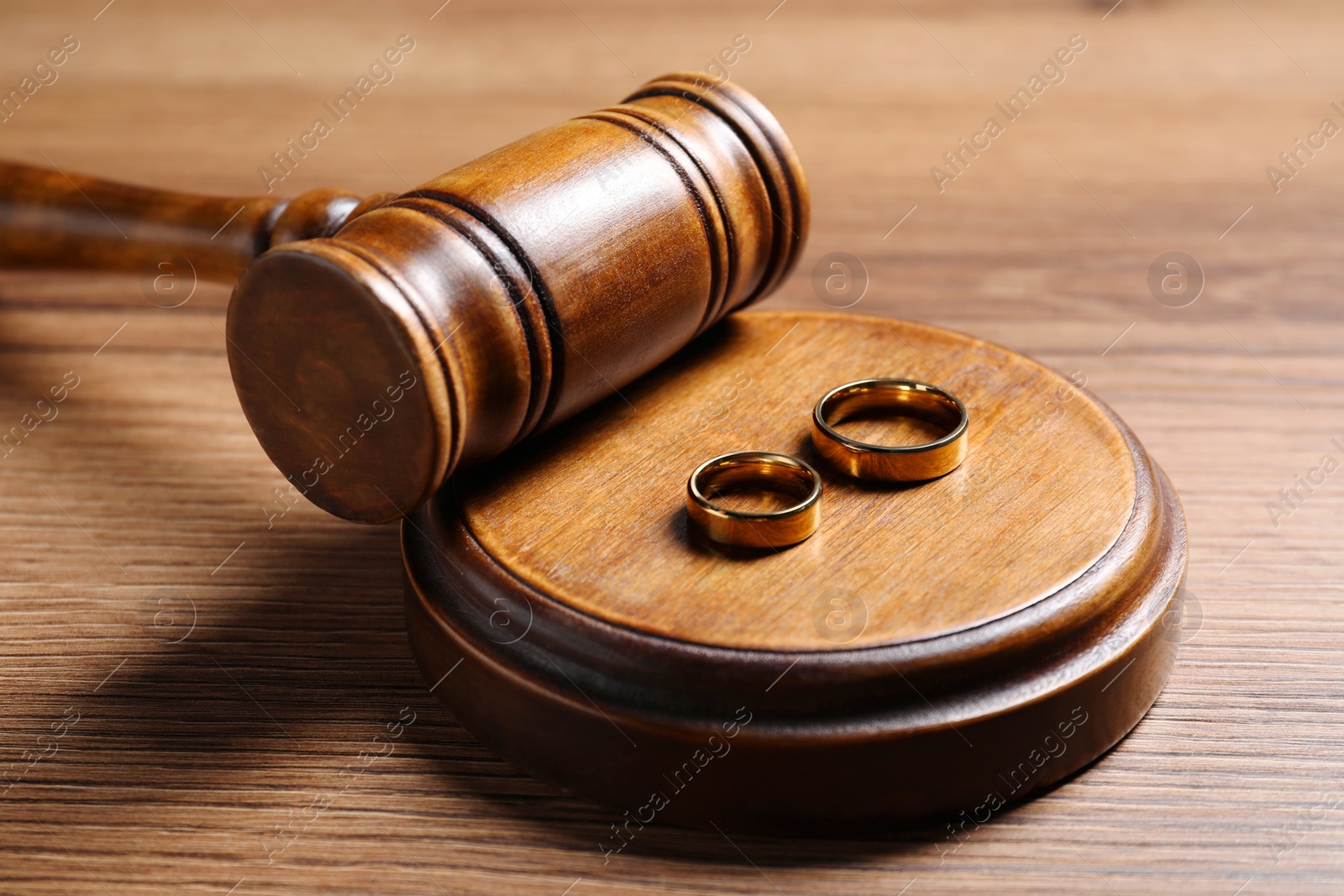 Photo of Divorce process. Gavel and wedding rings on wooden table, closeup