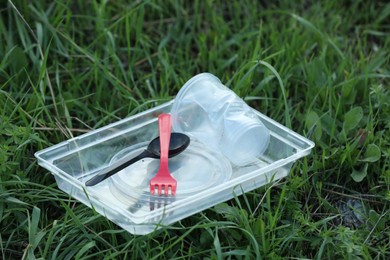 Photo of Used plastic tableware on grass outdoors. Environmental pollution concept