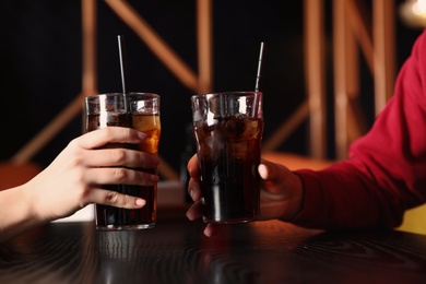 Young couple with glasses of refreshing cola at table indoors, closeup