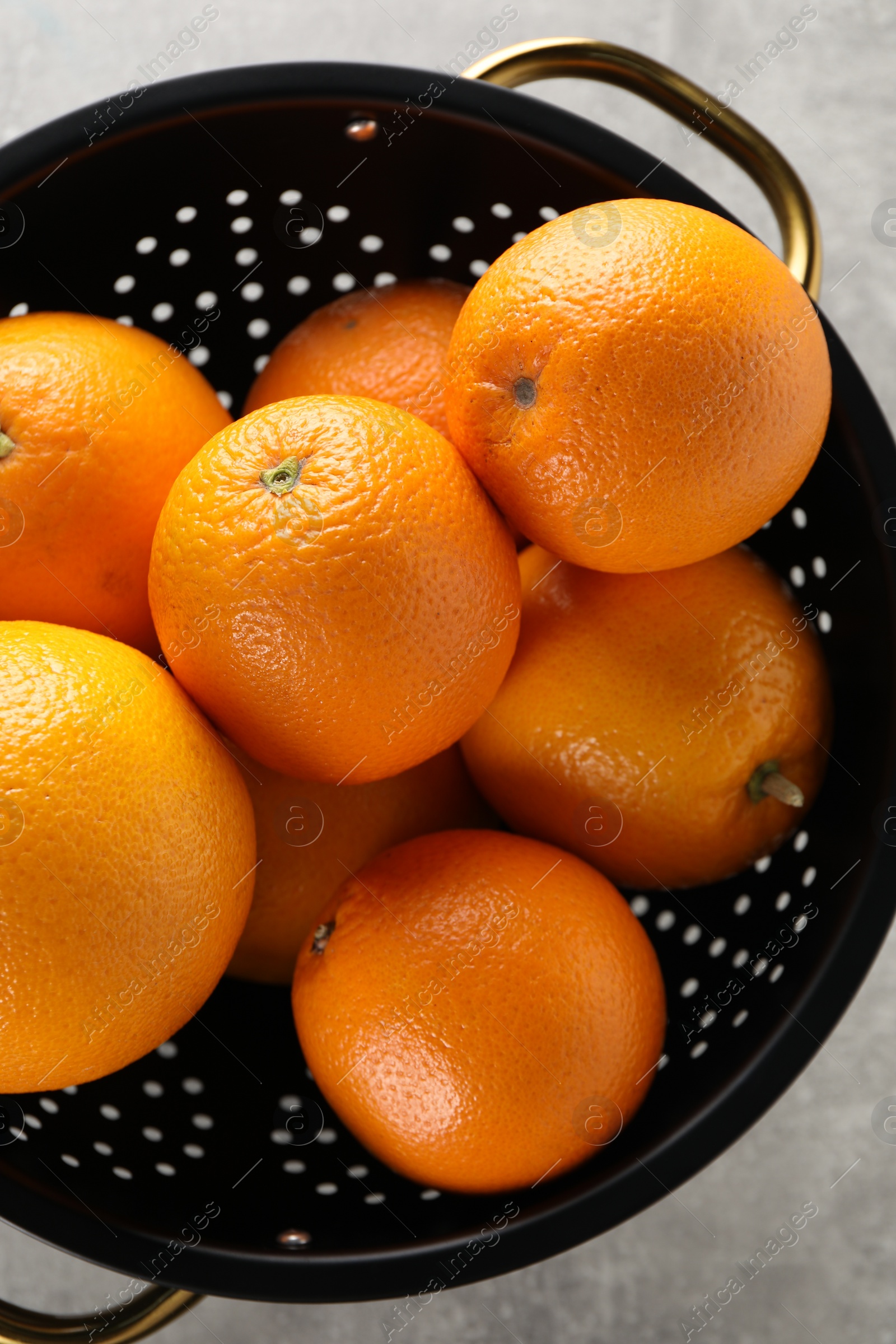 Photo of Fresh ripe oranges in black colander on light grey table, top view