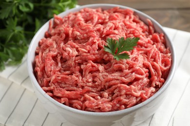 Photo of Raw ground meat in bowl and parsley on table, closeup